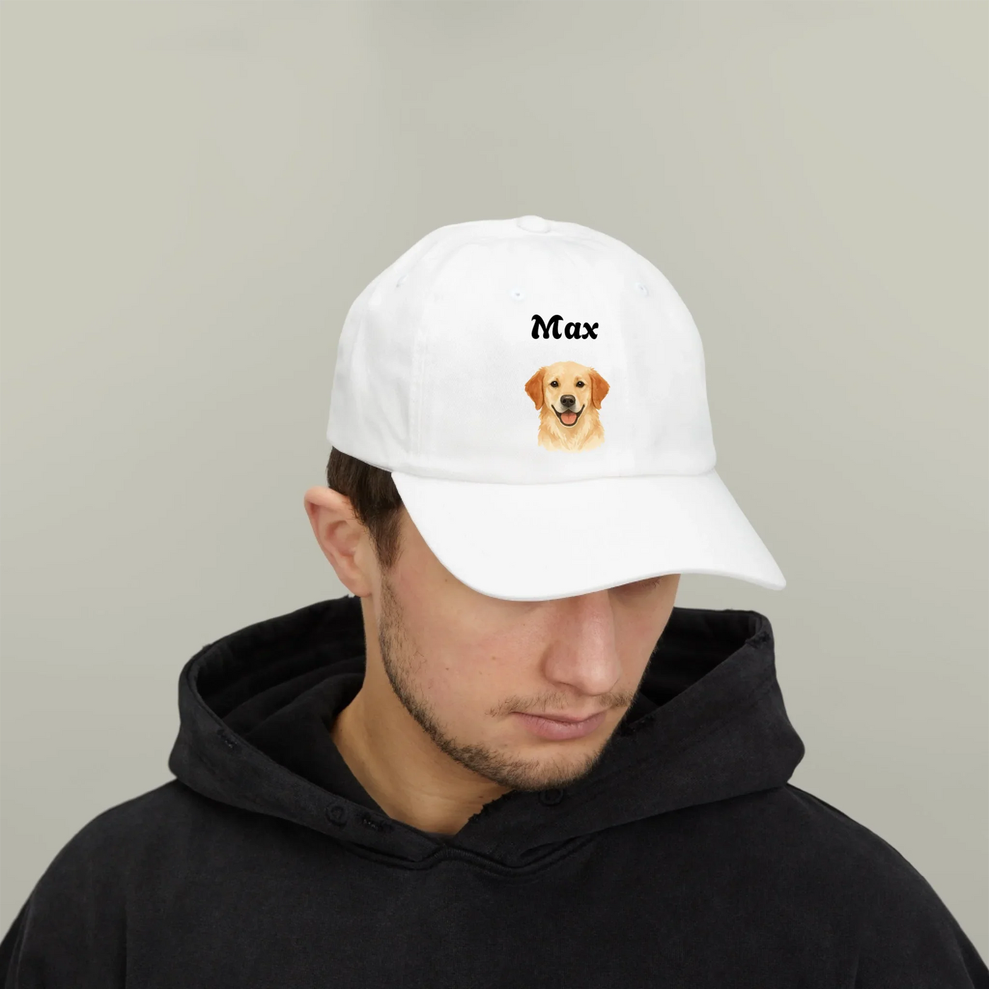 White classic dad cap with "Max" text and dog graphic worn by man in black hoodie